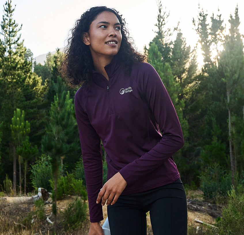 Person wearing a purple North Ridge quarter-zip baselayer in a forest setting, highlighting technical outdoor layering apparel.